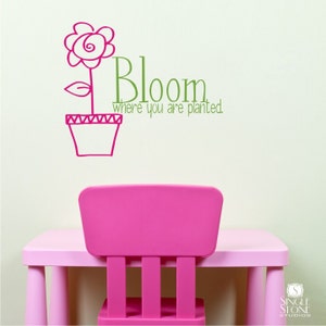 May include: Pink flower in a pot with the text "Bloom where you are planted."  The flower is drawn in a simple, childlike style. The text is in green and the flower is in pink.