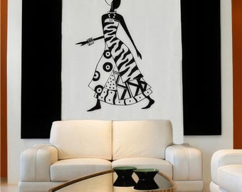 May include: A black and white wall art piece depicting a stylized figure in a patterned dress. The figure is walking, with a zebra stripe pattern on the dress. Two black rectangular panels flank the artwork, above a white sofa and a coffee table.