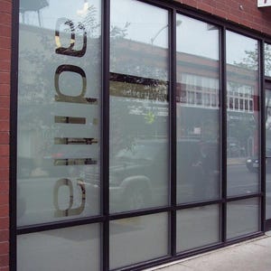 May include: Exterior view of a storefront with large glass windows and a brick facade. The word "glide" is displayed in large, frosted lettering on the glass. The windows reflect the street scene outside.