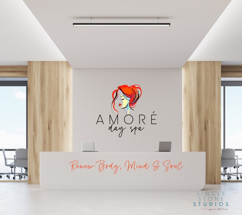 Pu&ograve; includere: Un bancone di reception bianco con un logo per una spa diurna chiamata "AMOR&Eacute; day spa" con un'immagine stilizzata di una donna con i capelli rossi. Il testo "Renew Body, Mind & Soul" &egrave; scritto sotto il logo. Il bancone si trova in un ufficio moderno con pannelli in legno e una finestra.