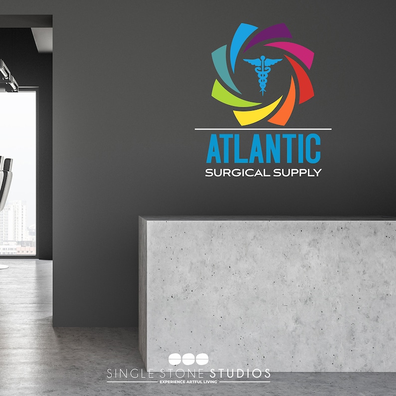 Pu&ograve; includere: Un logo colorato con un simbolo medico al centro, circondato da un vortice di colori arcobaleno. Il testo "ATLANTIC SURGICAL SUPPLY" &egrave; sotto il logo. Il logo &egrave; su una parete grigia, con un bancone in cemento di fronte. Il testo "SINGLE STONE STUDIOS EXPERIENCE ARTIFUL LIVING" &egrave; sotto il bancone.