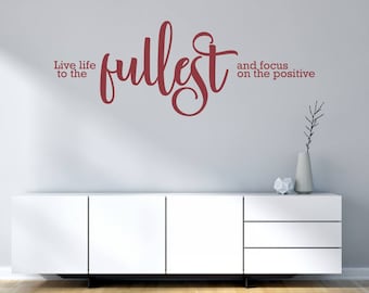 May include: A white wall with a burgundy vinyl wall decal that reads "Live life to the fullest and focus on the positive". The decal is above a white dresser with three drawers.