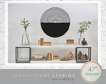 May include: Black and white geometric wall decal with a 47 inch diameter. The decal is a half circle with concentric lines and a solid black bottom half. The decal is displayed on a white wall above a white shelf with books and decorative objects.