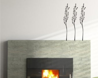 Könnte beinhalten: Ein moderner Kamin mit schwarzem Rahmen und einem knisternden Feuer. Der Kamin steht vor einer hellgrauen Wand mit einer schwarzen Silhouette von drei stilisierten Bäumen.
