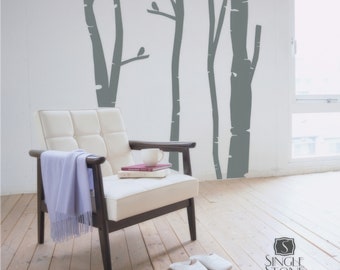 May include: A white armchair with a light blue throw blanket sits in a room with a light gray wall featuring a gray silhouette of a birch tree forest with birds.