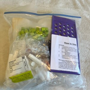 Peut inclure: Un sac en plastique transparent contenant un kit de fabrication de baume à lèvres. Il comprend un plateau de remplissage en plastique violet, un paquet de tubes torsadés blancs étiquetés 100 pack, des bouchons vert citron et une notice How to Use.