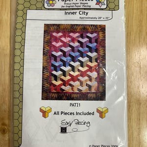 May include: A Paper Pieces quilt pattern kit titled Inner City, measuring approximately 28 inches by 35 inches. The package features a colorful geometric cube design, the text All Pieces Included, Easy Piecing, and a copyright date of 2009.