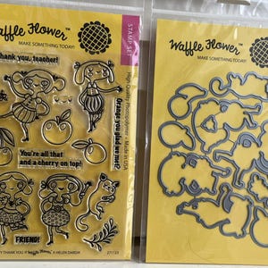 May include: Two clear stamp sets and dies on yellow backing. One set includes stamps with the text "Thank you, teacher!" and "You're all that and a cherry on top!" with illustrations of girls, fruit, and a cat. The other set is a die set.