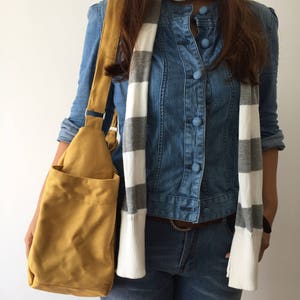May include: A mustard yellow canvas tote bag with a long strap. The bag is being held by a person wearing a denim shirt and jeans.