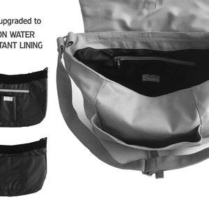 May include: Gray messenger bag with a black nylon water-resistant lining. The bag has a flap closure, a shoulder strap, and multiple pockets, including a zippered interior pocket. The text "Now upgraded to NYLON WATER RESISTANT LINING" is visible.
