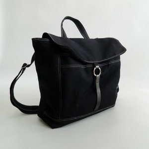 May include: A black backpack with a flap closure and a top handle. The bag features white stitching details and a leather strap with a metal ring. The straps are adjustable.