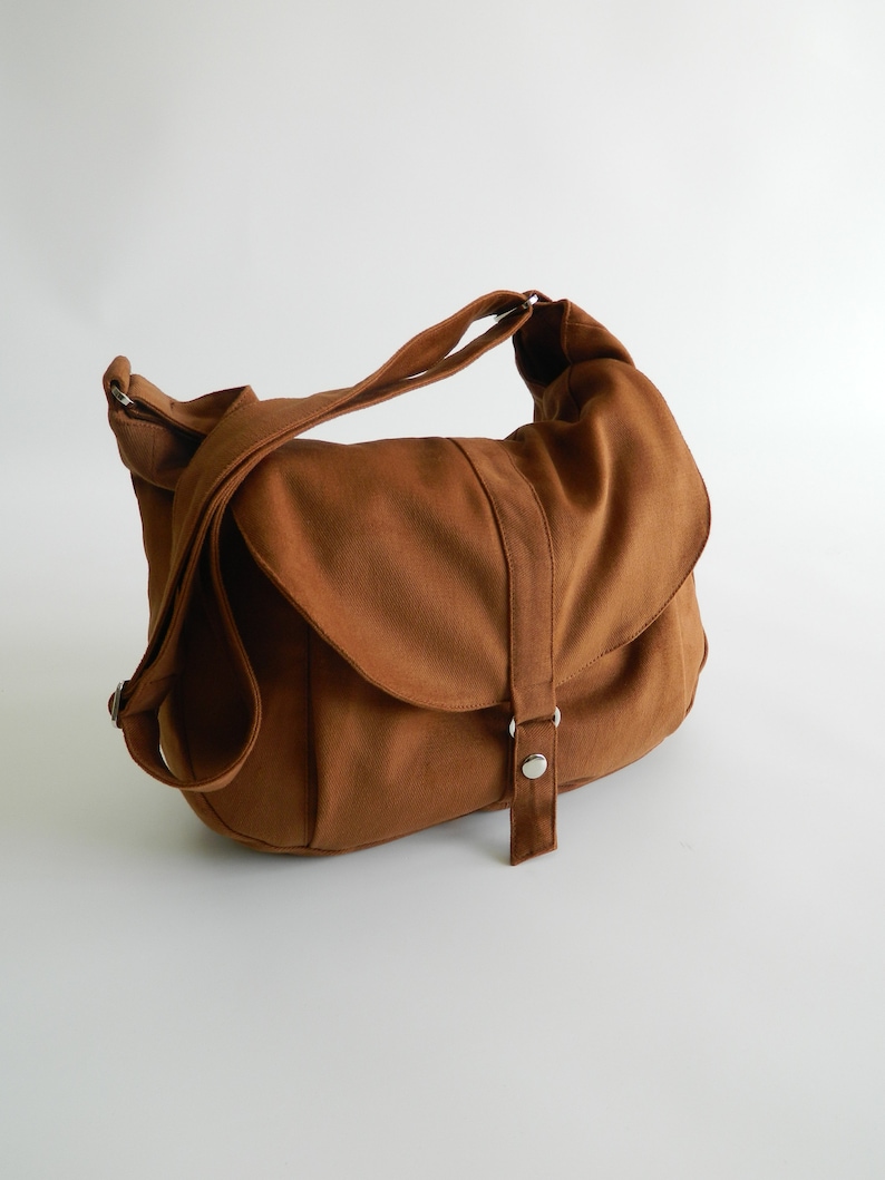 May include: A brown canvas messenger bag with a flap closure and adjustable shoulder strap. The bag features a buckle closure and a spacious interior, suitable for carrying various items. The bag is made of a durable material and is designed for everyday use.