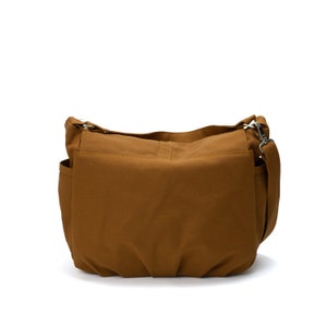 K&ouml;nnte beinhalten: Eine braune Umh&auml;ngetasche mit Schulterriemen und mehreren Taschen. Die Tasche ist aus einem robusten Stoff gefertigt und verf&uuml;gt &uuml;ber silberfarbene Metallbeschl&auml;ge. Die Tasche ist zum Tragen &uuml;ber der Schulter konzipiert.
