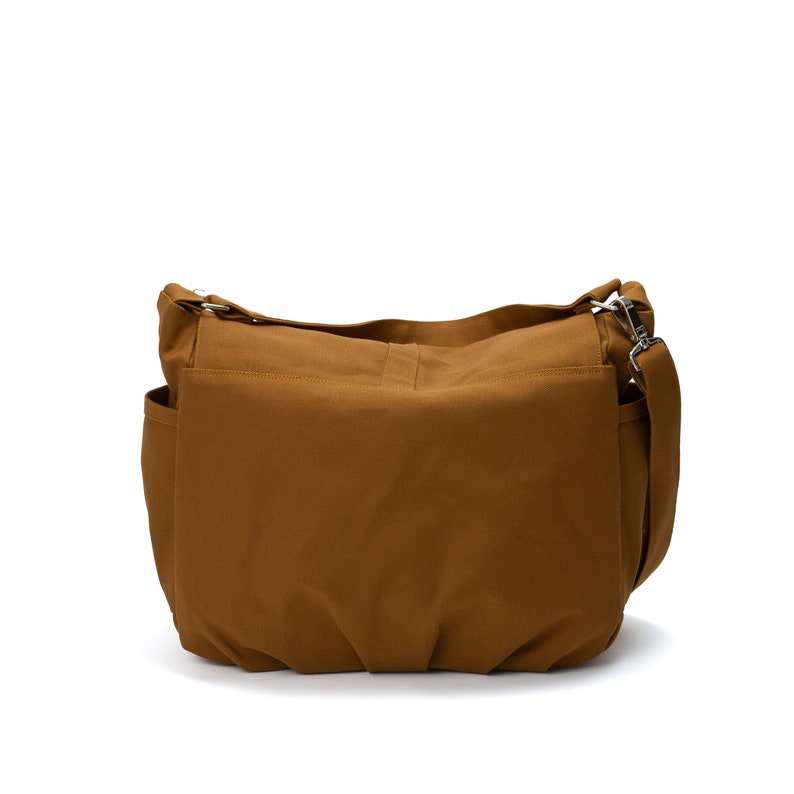K&ouml;nnte beinhalten: Eine braune Umh&auml;ngetasche mit Schulterriemen und mehreren Taschen. Die Tasche ist aus einem robusten Stoff gefertigt und verf&uuml;gt &uuml;ber silberfarbene Metallbeschl&auml;ge. Die Tasche ist zum Tragen &uuml;ber der Schulter konzipiert.