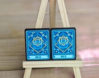May include: Two blue and gold pixel art cards with the word "HEX" printed on them. The cards are displayed on a small wooden easel.