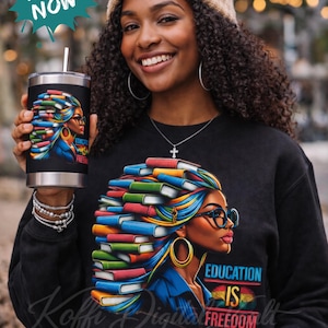 May include: A black sweatshirt and tumbler featuring a graphic of a woman with books in her hair, glasses, and the text "Education is Freedom." The tumbler has a silver lid and a white straw. The image also includes a beige beanie.
