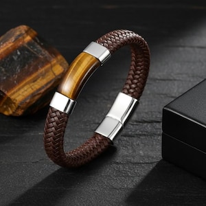 May include: Brown braided leather bracelet with a tiger's eye stone center and silver-tone metal accents. The bracelet is a stylish accessory, suitable for everyday wear. The bracelet's diameter is approximately 2.5 inches.