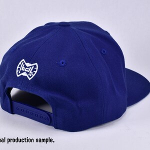 May include: A royal blue baseball cap with a white embroidered logo that says "1ball".