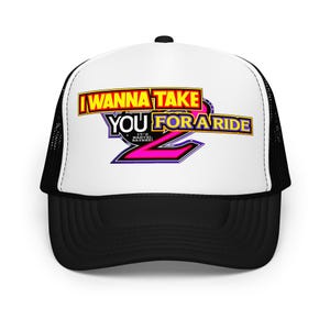 May include: A black and white trucker hat with the text "I WANNA TAKE YOU FOR A RIDE 2" in yellow, purple, and pink. The hat has a white front panel and a black mesh back, with a black brim.