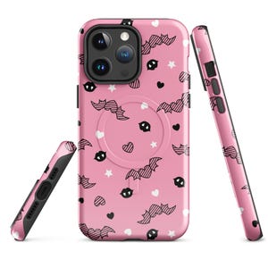 May include: Pink phone case with a black and white bat and heart pattern. The case has a built-in ring holder.