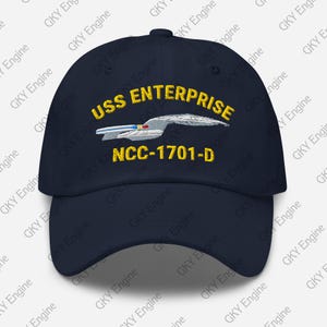 Könnte beinhalten: Marineblaue Baseballkappe mit gesticktem Text "USS ENTERPRISE NCC-1701-D" in Gold und Weiß. Die Kappe hat einen gebogenen Schirm und einen Knopf oben, ideal für Science-Fiction-Fans.