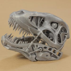 May include: A 3D printed model of a dinosaur skull with a detailed, intricate design. The skull is open, revealing the inner workings of the jaw and teeth.