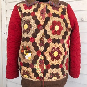 Peut inclure: Une veste matelassée avec un motif géométrique brun, rouge et jaune. La veste a un col brun et des manches rouges.