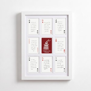 Könnte beinhalten: Ein gerahmtes Kunstwerk mit Spielkarten mit personalisierten Botschaften. Die Karten sind in einem Raster angeordnet, mit einer zentralen roten Karte mit den Namen und dem Datum eines Paares. Der Rahmen ist weiß.