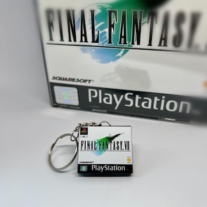 Può includere: Un portachiavi a forma di custodia per giochi PlayStation per Final Fantasy VII. Il portachiavi è bianco con accenti verdi e blu e il testo "FINAL FANTASY VII" e "PlayStation".