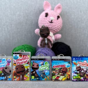 Puede incluir: Una colección de llaveros y figuras de ganchillo con temática de LittleBigPlanet. Los llaveros presentan portadas de juegos para PS3 y PS4. También hay un conejo de ganchillo rosa y un Sackboy de ganchillo marrón, junto con ovillos de lana.