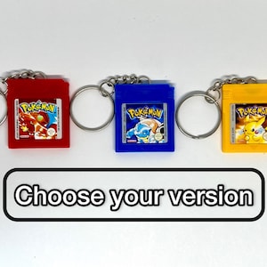 May include: Three Pokemon Game Boy cartridge keychains. The keychains are red, blue, and yellow. Each keychain features a different Pokemon character. Choose your version.
