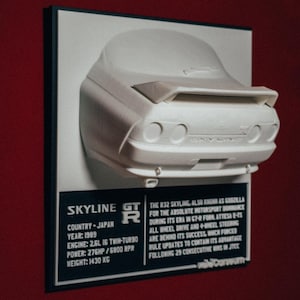 May include: A white model car of a Nissan Skyline GT-R, with a black plaque underneath that reads "SKYLINE GT-R", "COUNTRY - JAPAN", "YEAR: 1989", "ENGINE: 2.5L 16 Twin-Turbo", "POWER: 276HP / 5800 RPM", "WEIGHT: 1430 KG", and a description of the car's history and racing success.