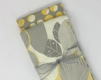 Puede incluir: Un conjunto de dos cuadrados de tela con un patrón geométrico gris y amarillo. Los cuadrados de tela están atados con una cinta gris y tienen una etiqueta blanca con el texto "Lilac & Lollipops" y una dirección de sitio web.