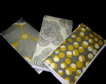 Puede incluir: Tres cuadrados de tela con diferentes patrones. El primer cuadrado tiene un diseño de flor grande, gris y amarilla. El segundo cuadrado tiene un fondo blanco con un patrón de remolino gris y amarillo. El tercero tiene un fondo gris con un patrón de círculo amarillo.
