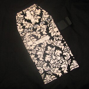 May include: A black and white fabric pouch with a damask pattern. The pouch has a flap closure and a black strap.