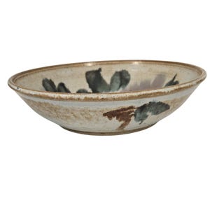 May include: A handmade ceramic bowl with a wide rim. The bowl features a cream-colored base with abstract floral designs in shades of green and brown. The rim has a darker, earthy tone, adding to its rustic charm.