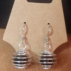 May include: A pair of silver wire wrapped earrings with black gemstone beads. The earrings are dangling and have a spiral design.