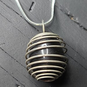 May include: A silver chain necklace with a black stone pendant encased in a silver wire cage.