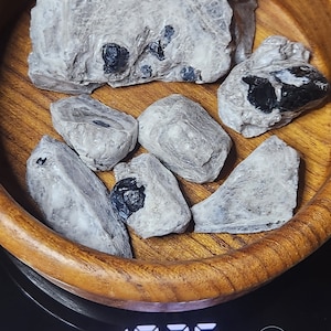 May include: A wooden bowl filled with seven grey and black stones, sitting on a digital scale that reads 1.036 lb.