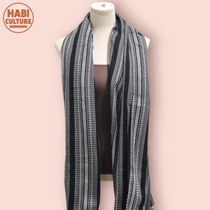 May include: A black and white striped scarf displayed on a mannequin. The scarf has vertical stripes with a detailed geometric design. The "HABI CULTURE" logo is in the top left corner. The background is a soft pink.