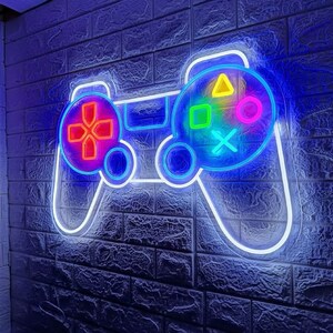 Può includere: Un'insegna al neon a forma di controller per videogiochi, con un contorno bianco e pulsanti colorati. Il controller è montato su un muro di mattoni scuri, illuminato da una luce blu.