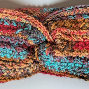 May include: A hand-crocheted headband in a twisted design. The headband features a mix of colors, including teal, red, orange, and brown. The yarn has a textured appearance, and the headband is likely made of a soft, warm material.