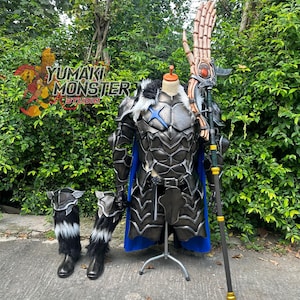 May include: A full suit of armour with a blue cape, displayed on a mannequin. The armour is dark grey with black accents and a blue star design. A matching spear and boots with fur trim are also included. The logo "YUMAKI MONSTER STUDIO" is visible.