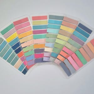 May include: A collection of colorful sticky note pads arranged in a fan shape. The pads are in various pastel shades, including pink, blue, green, yellow, and orange. They are neatly organized in clear plastic holders, ideal for office or school use.