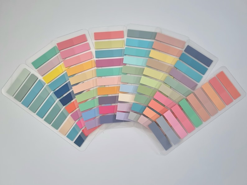 May include: A collection of colorful sticky note pads arranged in a fan shape. The pads are in various pastel shades, including pink, blue, green, yellow, and orange. They are neatly organized in clear plastic holders, ideal for office or school use.