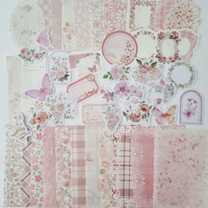 Op de afbeelding: Een verzameling roze en wit scrapbookpapier, stickers en versieringen. De set bevat bloempatronen, vlinders, labels en frames. Het kleurenpalet is zacht en vrouwelijk, perfect voor knutsel- en journalingprojecten.