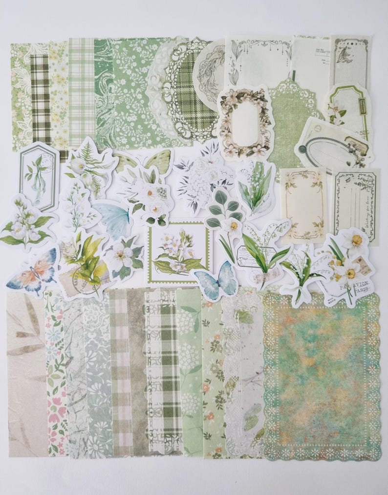 Op de afbeelding: Een verzameling groen en wit scrapbookpapier en uitgestanste versieringen. Het papier heeft bloemen-, ruit- en kanten patronen. Uitgestanste onderdelen zijn onder andere vlinders, bloemen en frames, voor knutsel- en journalingprojecten.