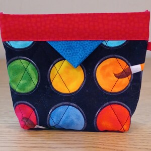 May include: A small black quilted pouch with a red top flap and a blue triangle flap. The pouch has a colorful paint splatter design with a paintbrush and a white handle.