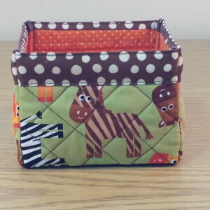 May include: A brown and green fabric storage bin with a polka dot pattern. The bin features a quilted design with animal illustrations, including a zebra, a giraffe, and a horse.