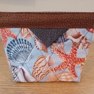 May include: A blue quilted fabric pouch with a brown top flap. The pouch features a seashell and starfish design.